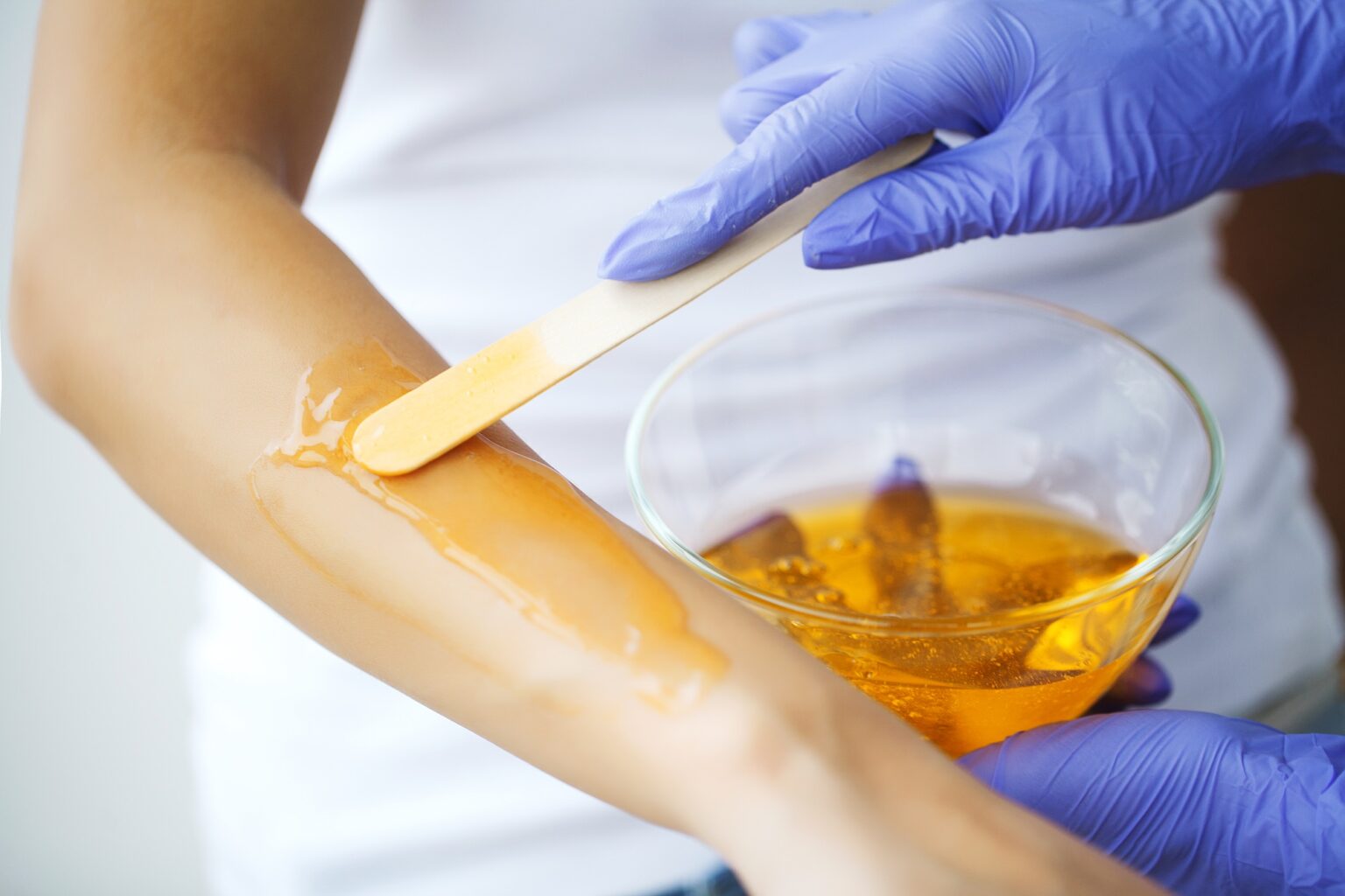 Master does epilation of hands with help of sugar paste hot wax in salon beauty.