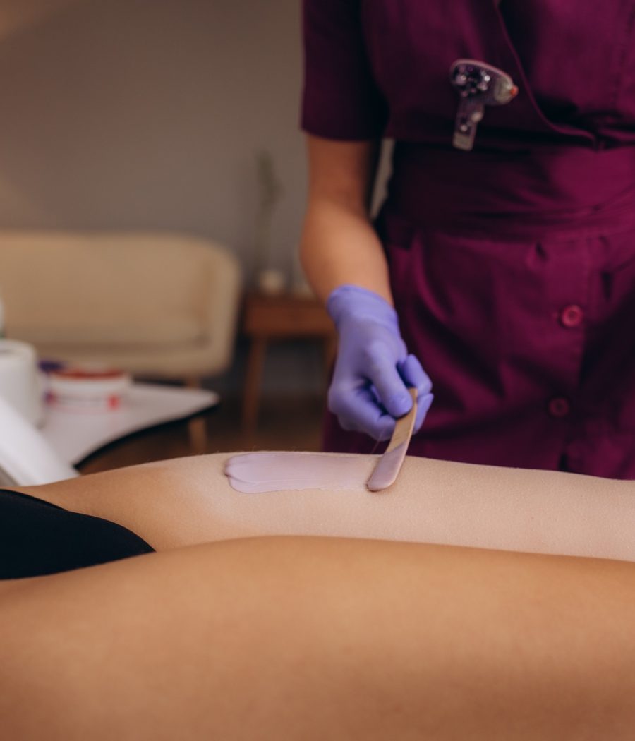 A master applies pink depilatory wax to a young woman's leg for hair removal. Depilation with wax.