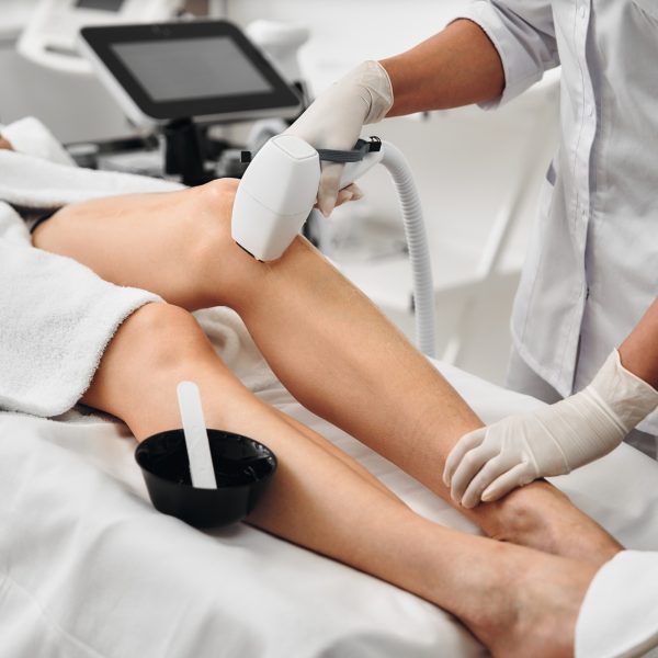Aesthetician performing laser hair removal on a clients leg in a clinic